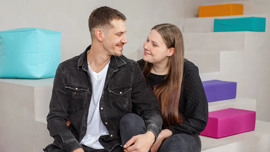 Tim Katzenbauer und Lavinia Wollny sitzen für ein Fotoshooting auf einer Treppe. Hinter ihnen sind bunte Elemente.