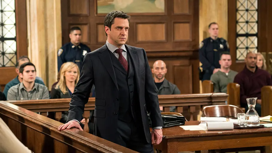 Law & Order: Speical Victims Unit Rafael Barba steht als Staatsanwalt im Gerichtssaal und blickt während einer Verhandlung entschlossen nach vorne. Im Hintergrund sitzen Richter, Geschworene, Zuschauer und Polizeibeamte – Szene aus „Law & Order: Special Victims Unit“.