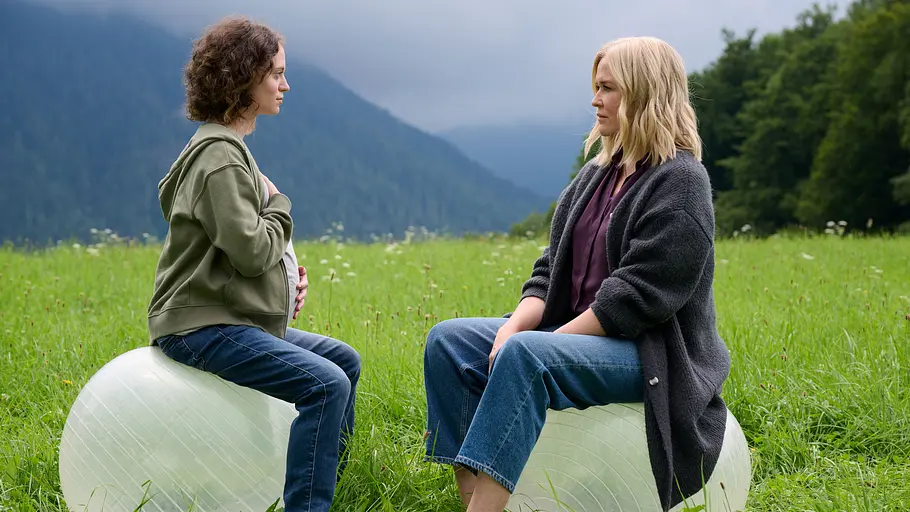 Lena Lorenz Auf einer Wiese in den Bergen sitzen sich Sina Schumacher (Fanny Altenburger) und Lena Lorenz (Judith Hoersch) auf großen Gymnastikbällen gegenüber. Sina legt eine Hand auf ihren Bauch, die andere auf ihre Brust Beide blicken sich ernst an.