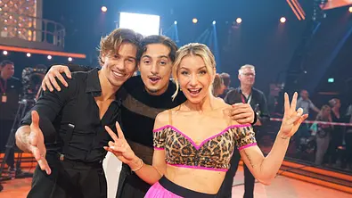 Joel Mattli, Milano und Anna-Carina Witschack stehen eng beieinander auf einer beleuchteten Tanzfläche und lächeln in die Kamera. - Foto: RTL / Stefan Gregorowius