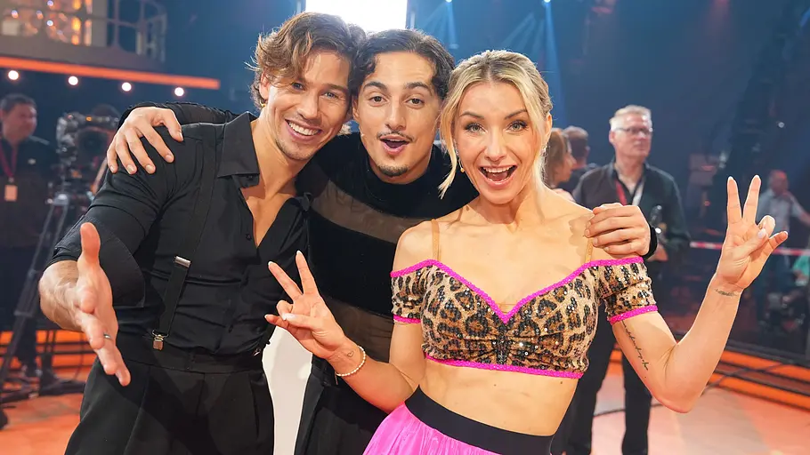 Joel Mattli, Milano und Anna-Carina Witschack Joel Mattli, Milano und Anna-Carina Witschack stehen eng beieinander auf einer beleuchteten Tanzfläche und lächeln in die Kamera.