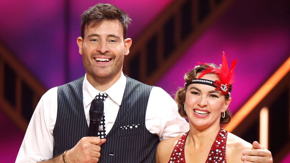 „Let’s Dance“ bald ohne Renata Lusin? Marc Eggers lacht und legt den Arm um Renata Lusin, die ein Haarband mit roter Feder darin trägt und etwas gequält schaut