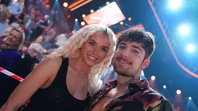 Kim und Willi lächeln gemeinsam in die Kamera im Publikum einer „Let’s Dance“-Live-Show, im Hintergrund Studio-Lichter und Zuschauer. - Foto: RTL / Stefan Gregorowius