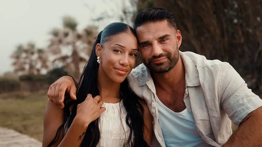 Aleks und Vanessa Vanessa und Aleks Petrovic sitzen eng nebeneinander im Freien und lächeln in die Kamera. Aleks hat den Arm um Vanessa gelegt, während beide entspannt für die Aufnahme posieren.