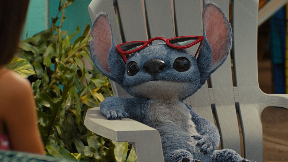 Stitch sitzt auf einem Stuhl und hat seine Sonnenbrille auf die Stirn geschoben.