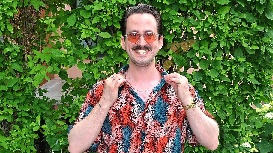 Marti Fischer posiert beim ZDF Fernsehgarten mit Sonnenbrille und sieht sein Shirt auseinander.