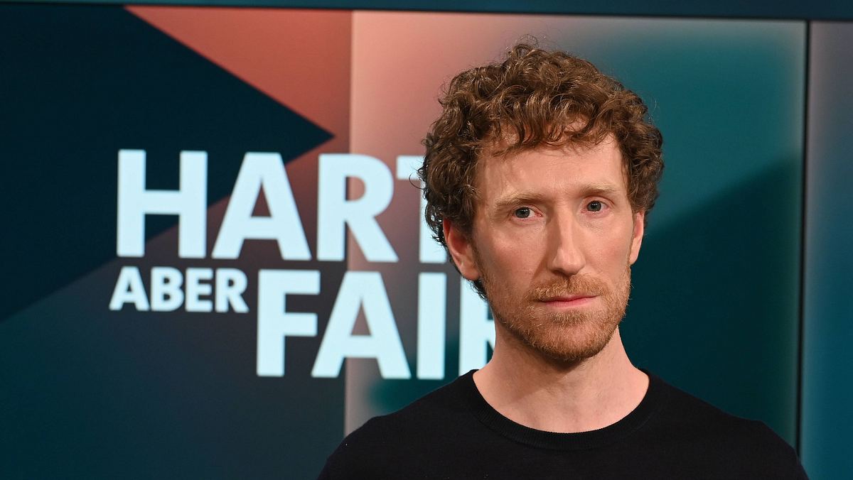 Louis Klamroth kriegt neuen Job Louis Klamroth steht in einem schwarzen Oberteil vor dem „Hart aber fair“-Logo.