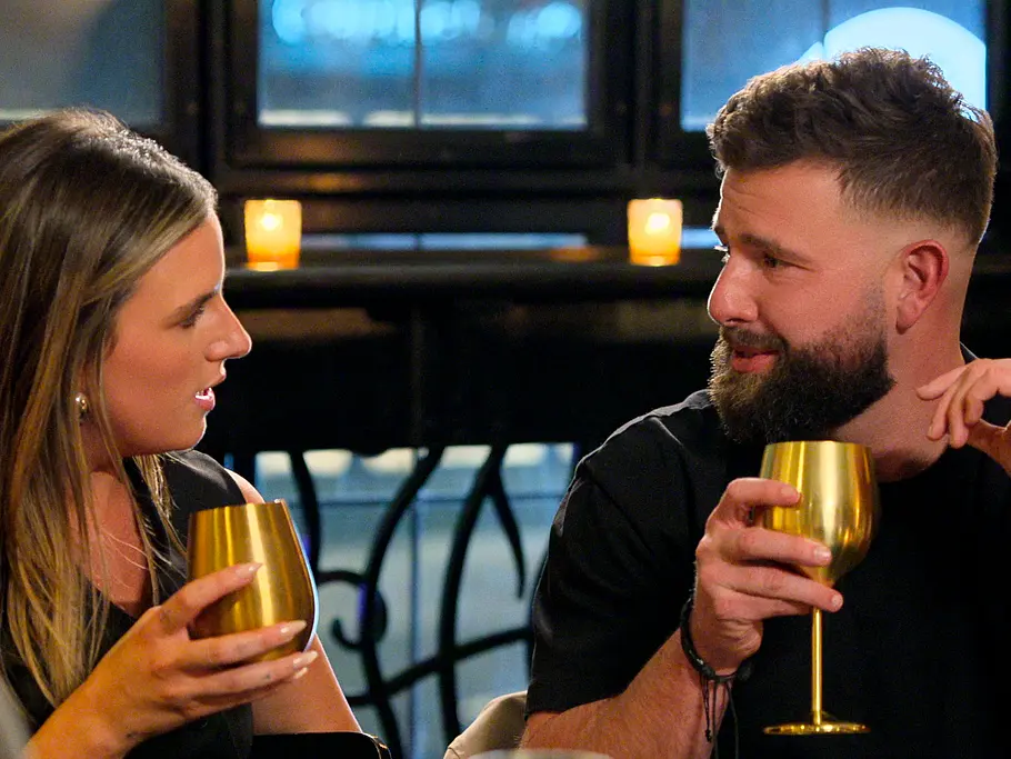 Michaella und Rob sind getrennt „Love is Blind:Boston“: Michaella und Rob sitzen einander zugewandt mit goldenen Kelchen in den Händen. Im Hintergrund leuchten Kerzen.