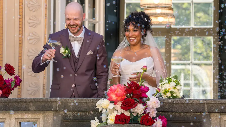 Gunnar und Josy prosten ihren Gästen nach ihrer Love is Blind-Traumhochzeit zu, es fliegen Seifenblasen.