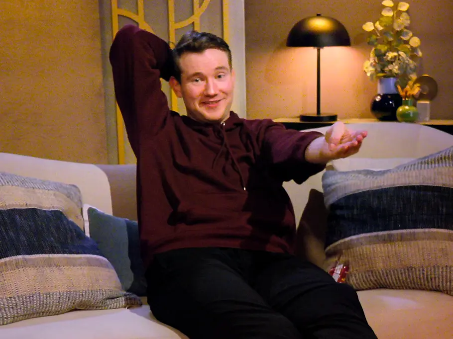 Morrey Eglin sitzt auf einem beigen Sofa, legt die Füße auf einen Hocker und hält einen Arm hinter den Kopf.
