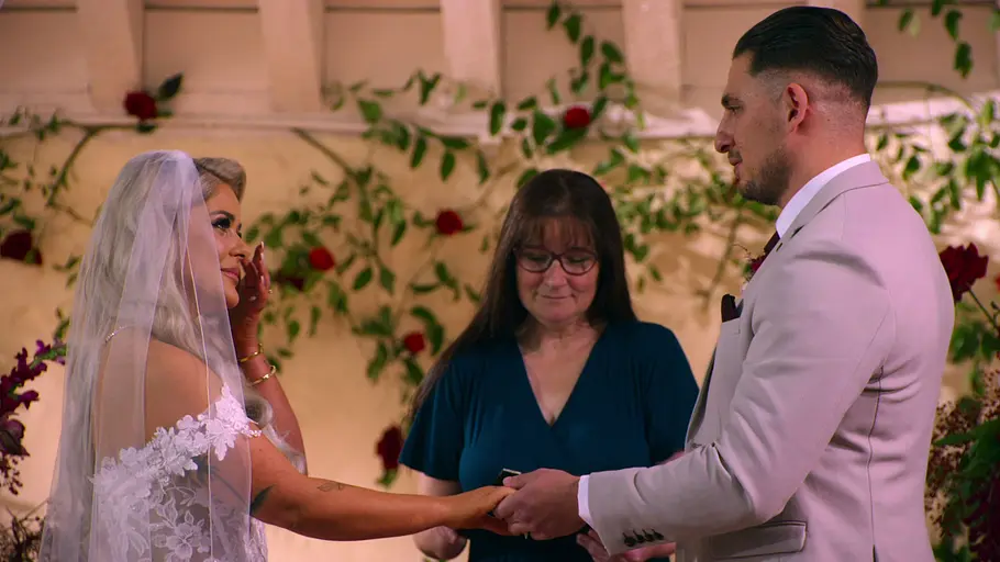 Bardha und Jed stehen vor dem Altar und halten Händchen.