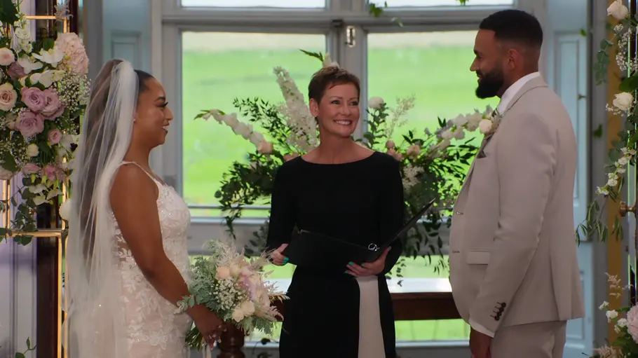 Demi und Ollie stehen vor dem Altar und lächeln sich an.