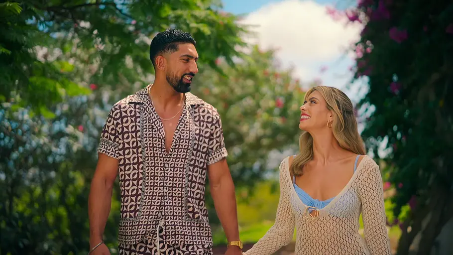 Ajay und Ciara gehen Hand in Hand durch einen Garten und schauen sich lächelnd an.