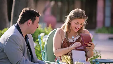 David Isaacman und Abbey Romeo sitzen in der Öffentlichkeit. Romeo freut sich über ein Geschenk.  - Foto: Courtesy of Netflix/© 2025 Netflix, Inc.