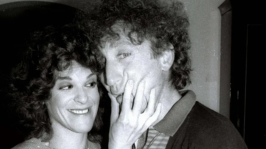 Gilda Radner und Gene Wilder posieren auf einer Schwarz-Weiß-Aufnahme eng nebeneinander, während sie ihm lächelnd die Wange hält.