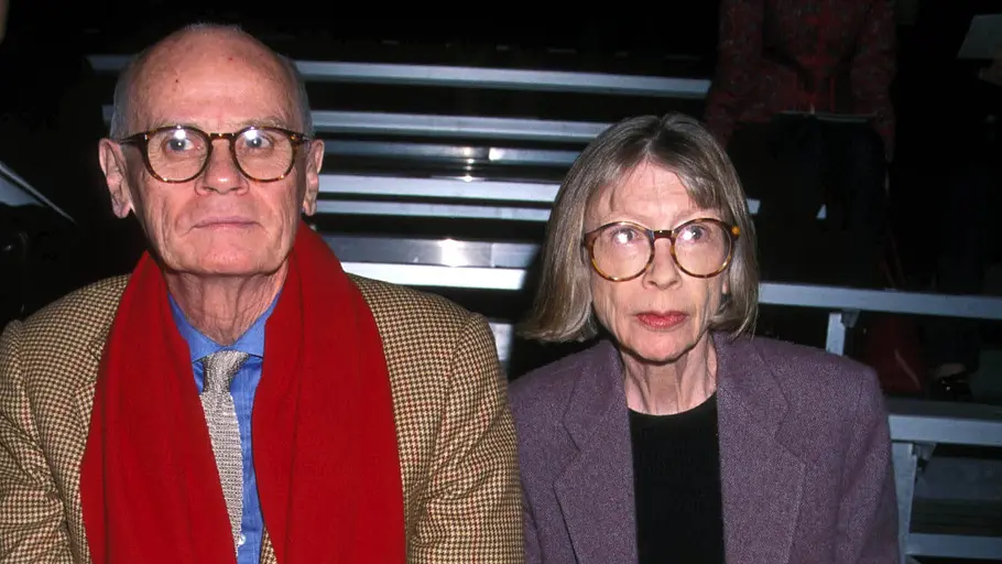 Joan Didion und John Gregory Dunne sitzen nebeneinander in der ersten Reihe einer Veranstaltung und blicken ernst nach vorn.