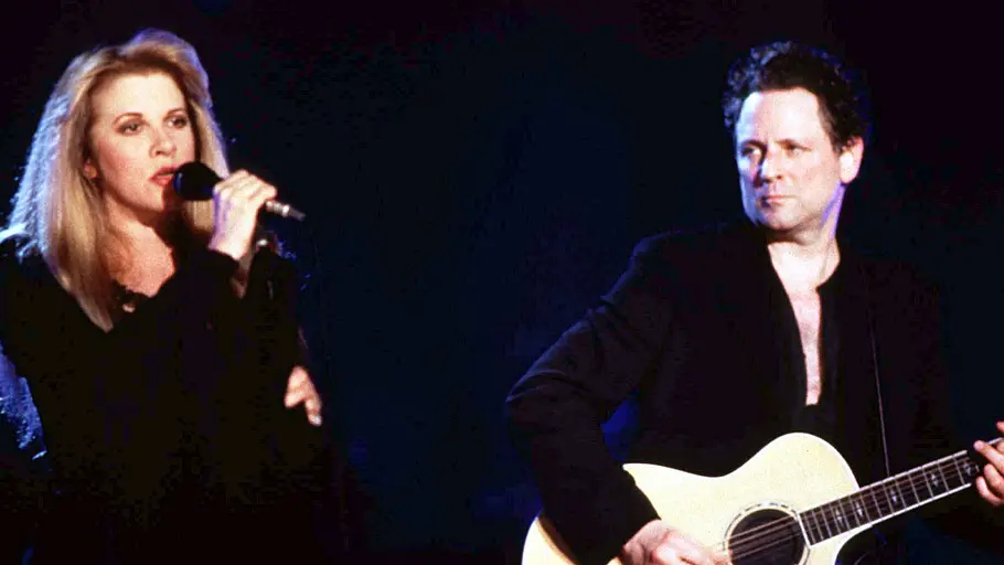 Stevie Nicks singt auf einer Bühne ins Mikrofon, während Lindsey Buckingham neben ihr Gitarre spielt und zu ihr hinüberschaut.