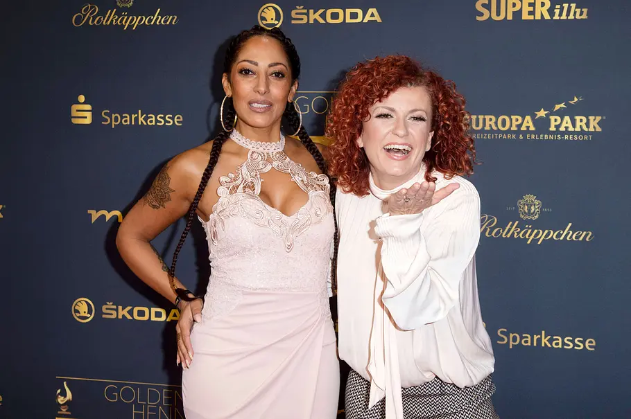 Lucy Diakovska und Jessica Wahls Lucy Diakovska und Jessica Wahls posieren vor einer Sponsorenwand: Jessica im rosa Spitzenkleid, Lucy mit roten Locken und weißer Bluse.
