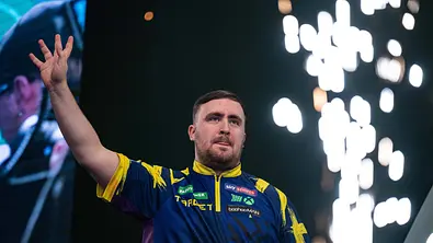 Luke Littler jubelt mit seiner rechten Hand bei der PDC-WM 2026. Im Hintergrund ist ein kleines Feuerwerk zu sehen! - Foto: IMAGO / Action Plus