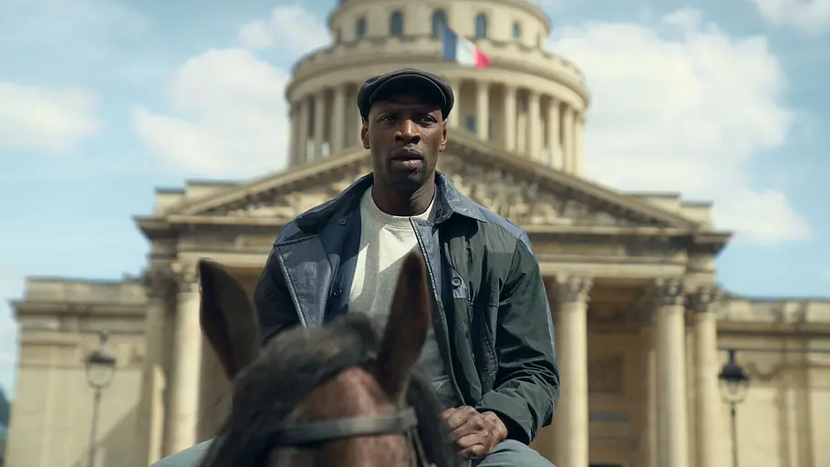 „Lupin“ Staffel 4 bietet noch mehr Action und soll auch Neueinsteiger begeistern. Assane Diop sitzt mit dunkler Schirmmütze auf einem Pferd vor einem Kuppelbau mit Säulen und französischer Flagge.