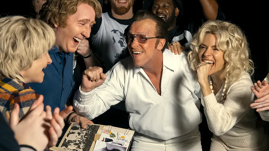 Kathryn Hahn, Nicolas Cage, Christian Bale und Sienna Miller lachen in einer Gruppe. Vor ihnen liegt ein offenes Fotoalbum.