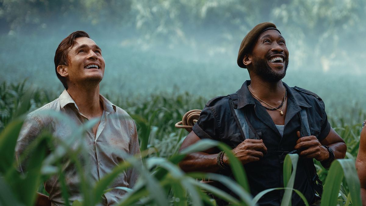 Mahershala Ali und Rupert Friend stehen in „Jurassic World: Die Wiedergeburt“ als Duncan Kincaid und Martin Krebs im Gras und schauen fasziniert nach oben. 