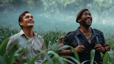 Mahershala Ali und Rupert Friend stehen in „Jurassic World: Die Wiedergeburt“ als Duncan Kincaid und Martin Krebs im Gras und schauen fasziniert nach oben.  - Foto: © Universal Studios