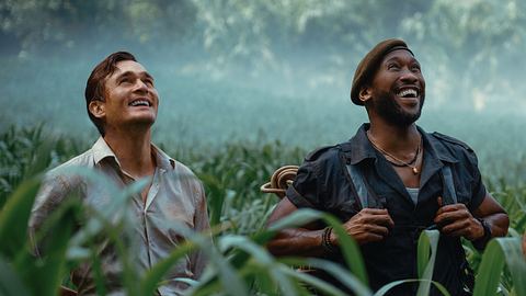 Mahershala Ali und Rupert Friend stehen in „Jurassic World: Die Wiedergeburt“ als Duncan Kincaid und Martin Krebs im Gras und schauen fasziniert nach oben.  - Foto: © Universal Studios