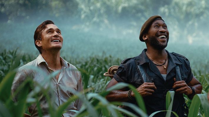 Mahershala Ali und Rupert Friend stehen in „Jurassic World: Die Wiedergeburt“ als Duncan Kincaid und Martin Krebs im Gras und schauen fasziniert nach oben.  - Foto: © Universal Studios