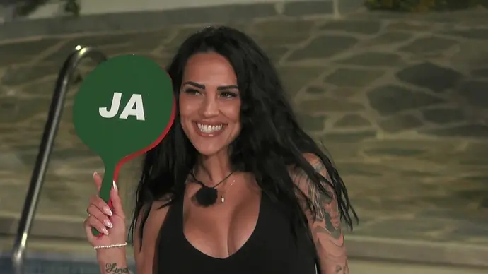 Elena Miras hält lächelnd ein grünes „Ja“-Schild in die Kamera, während sie am Pool der „Make Love, Fake Love“-Villa steht. - Foto: RTL