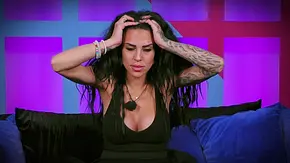Eine Frau mit langen dunklen Haaren sitzt auf einem Sofa und hält beide Hände an ihren Kopf. Sie trägt ein dunkles ärmelloses Oberteil, mehrere Armbänder und hat auffällige Tattoos an beiden Armen. Ihr Blick ist nach unten gerichtet und ihr Gesichtsausdruck wirkt nachdenklich oder angespannt. Im Hintergrund sind leuchtende violette und blaue geometrische Formen zu sehen, die an ein Studio- oder Fernsehset erinnern. - Foto: RTL