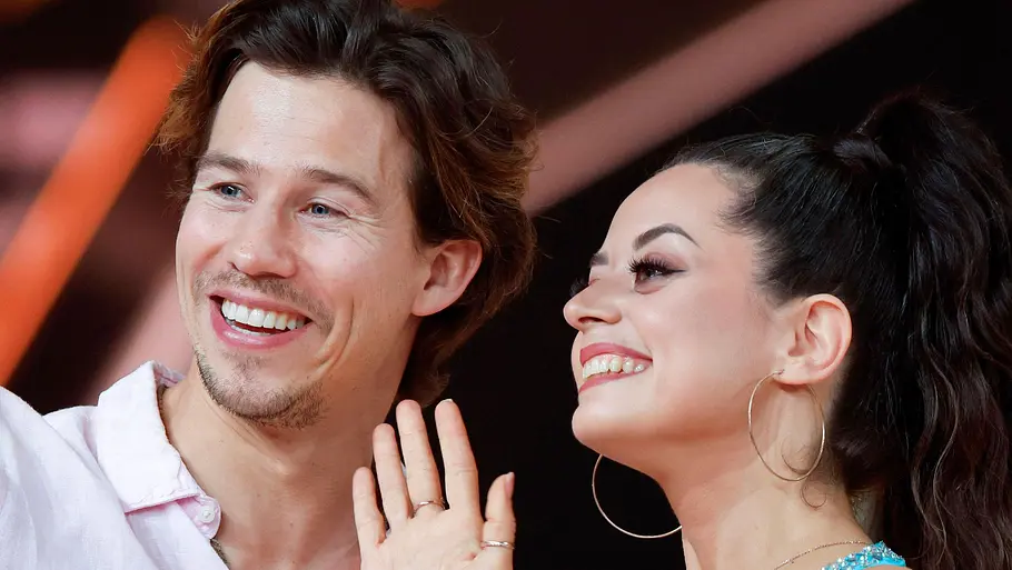 Malika Dzumaev und Joelv Mattli sind gemeinsam im Urlaub. Joel lächelt, während Malika in die Kamera winkt.