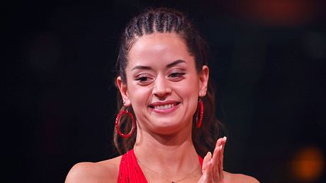 Malika Dzumaev mit geflochtenen Haaren und in einem roten Kleid schaut besorgt zu Boden. - Foto:  IMAGO / Panama Pictures