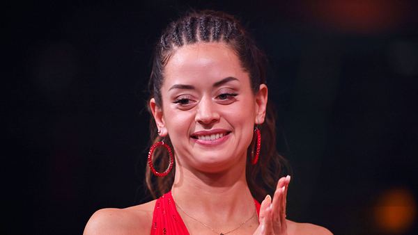 Malika Dzumaev mit geflochtenen Haaren und in einem roten Kleid schaut besorgt zu Boden. - Foto:  IMAGO / Panama Pictures