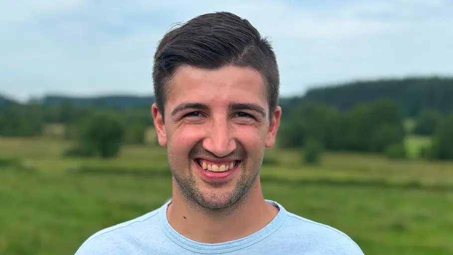 Manuel lächelt im blauen Shirt in die Kamera.