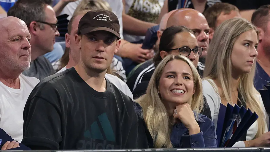 Manuel Neuer und seine Frau Anika Manuel Neuer mit dunklem Sweatshirt und Baseballkappe sitzt neben seiner Frau auf der Tribüne, beide blicken aufmerksam ins Stadion, umgeben von weiteren Zuschauern.