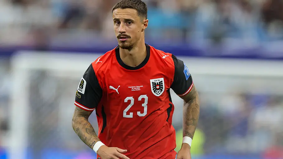Fußballspieler der österreichischen Nationalmannschaft im rot-schwarzen Trikot mit der Rückennummer 23 läuft während eines Länderspiels über den Rasen. Im Hintergrund sind das Tor und die verschwommenen Ränge des Stadions zu sehen.