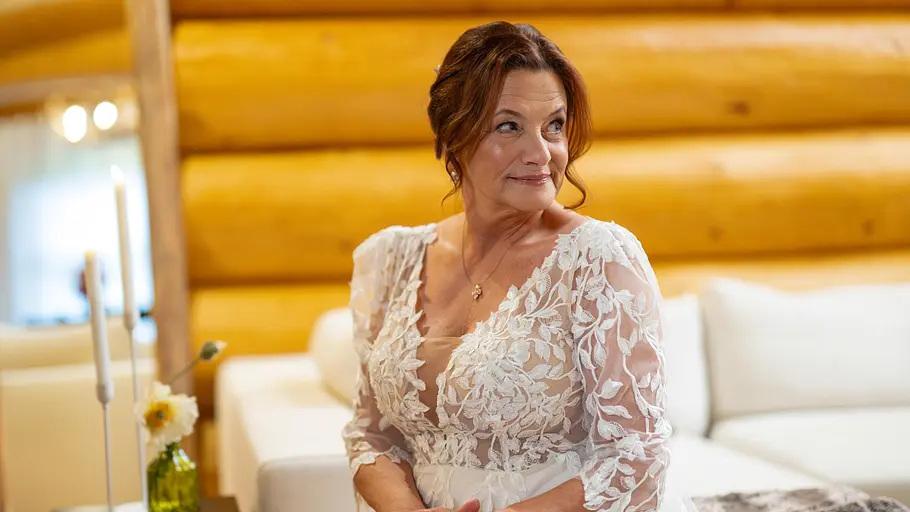 Marén Hochzeit auf den ersten Blick Marén trägt ein Brautkleid und sitzt auf einem Bett. Sie schaut lächelnd zur Seite.