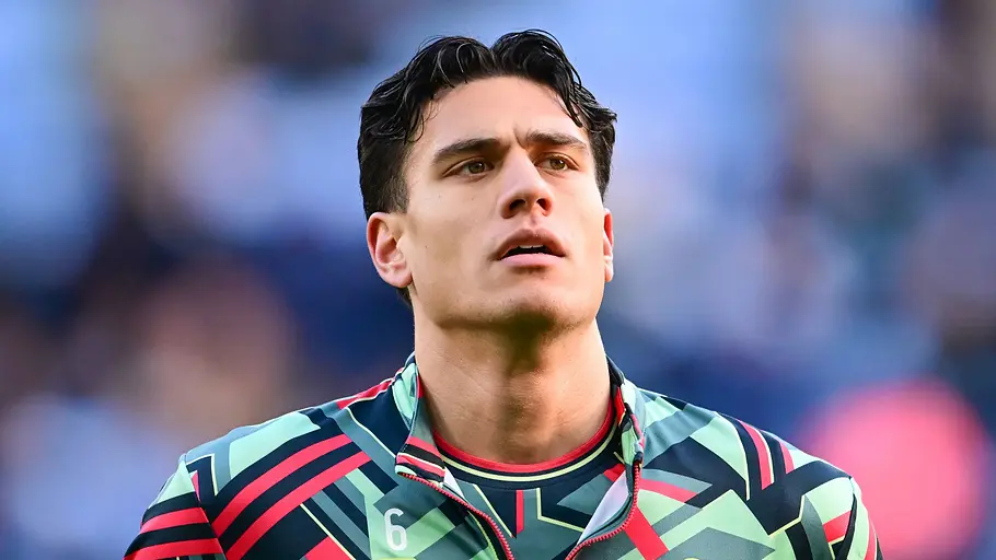 Fußballspieler von Swansea City im auffällig gemusterten Trainingsoberteil blickt vor einem Spiel konzentriert nach oben. Der Hintergrund des Stadions ist unscharf.