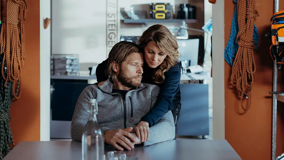 Markus wird von Katharina getröstet. Markus schaut traurig, während Katharina ihn von hinten umarmt.