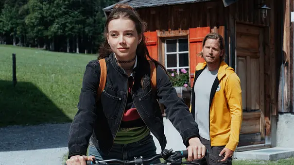 Mia hält im Vordergrund einen Fahrradlenker. Hinter ihr steht Markus in gelber Jacke vor einem Holzhaus mit roten Fensterläden. - Foto: ZDF/Sabine Finger Fotografie Mia hält im Vordergrund einen Fahrradlenker. Hinter ihr steht Markus in gelber Jacke vor einem Holzhaus mit roten Fensterläden. - Foto: ZDF/Sabine Finger Fotografie