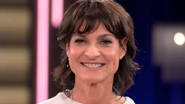 Porträt einer lächelnden Frau mit kurzem dunklem Haar in einem TV-Studio mit unscharfem Hintergrund und Studiolicht. - Foto:  IMAGO / Rainer Unkel