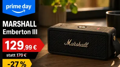 Ein schwarzer Marshall Emberton III Bluetooth-Lautsprecher steht auf einem Holztisch in einer warm beleuchteten Wohnumgebung. Links im Bild befindet sich eine Prime-Day-Grafik mit dem Produktnamen, dem Angebotspreis von 129,99 Euro, der durchgestrichenen UVP von 179 Euro sowie einem gelben Rabatt-Hinweis von 27 Prozent. - Foto: Chat GPT / TV Movie / Marshall