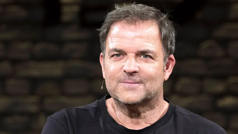 Martin Rütter Martin Rütter trägt ein schwarzes T-Shirt und ein Headset-Mikrofon vor einem dunklen, unscharfen Hintergrund.