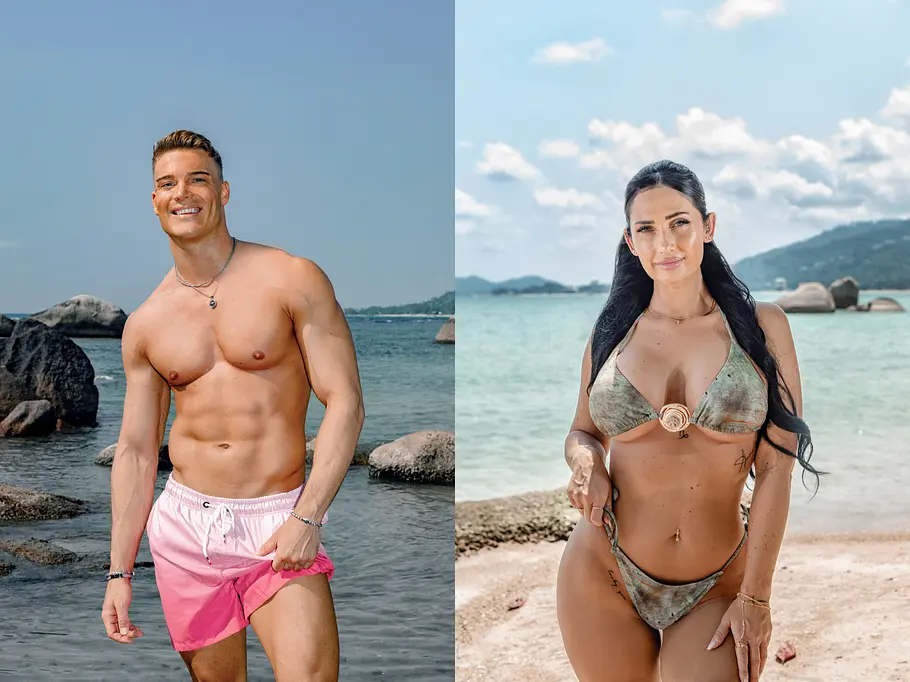 AYTO Ein junger, muskulöser Mann in pink-weißer Badehose steht lächelnd am Strand vor Felsen und Meer. Neben ihm posiert eine Frau mit langen dunklen Haaren im grünen Bikini am Sandstrand, beide blicken in die Kamera. Im Hintergrund sind türkisblaues Wasser und Himmel zu sehen.