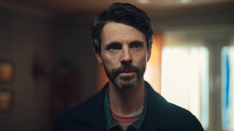 Carl Morck schaut leicht beunruhigt nach links, der Hintergrund ist unscharf. - Foto: Justin Downing/Netflix