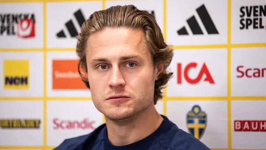 Fußballspieler der schwedischen Nationalmannschaft sitzt bei einer Pressekonferenz vor einer Sponsorenwand und blickt mit ernstem Gesichtsausdruck in die Kamera. Er trägt ein dunkelblaues Trainingsshirt mit dem schwedischen Verbandslogo.