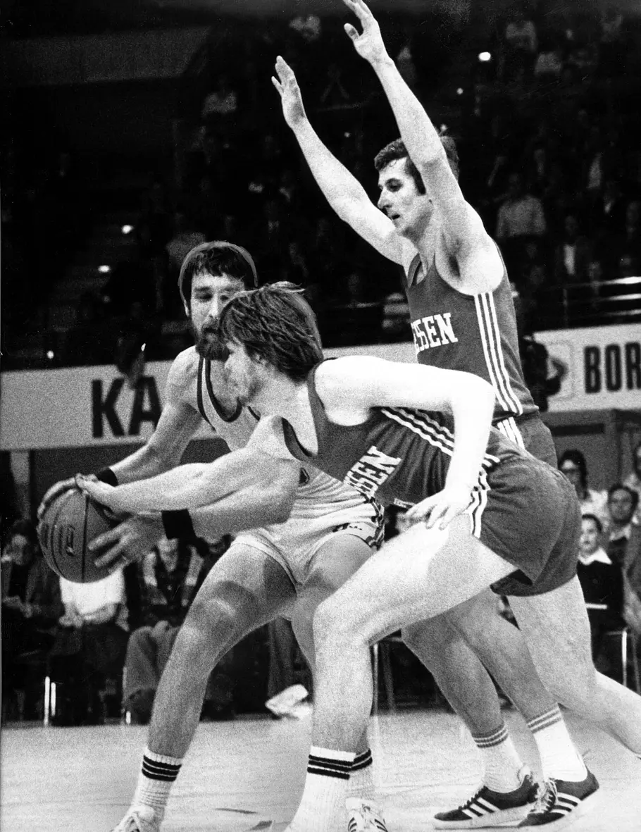 Matzi Strauss auf dem Basketball-Court Schwarz-Weiß-Bild von 1978 zeigt Matthias Strauss (Mitte) bei einem Spiel des TuS 04 Leverkusen gegen MTV Gießen mit Ecker (Leverkusen) und Gießen-Mitspieler Ampt um den Ball rangeln.