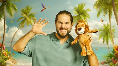 Reality-TV-Star Maurice Dziwak am Strand vor Palmenkulisse, mit gebleckten Zähnen und erhobener Handpose, in der anderen Hand ein Löwen-Stofftier. - Foto: Joyn