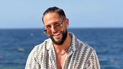 Maurice Dziwak sitzt lächelnd auf einem Geländer vor dem Meer - Foto: Instagram/@maurice_dziwak